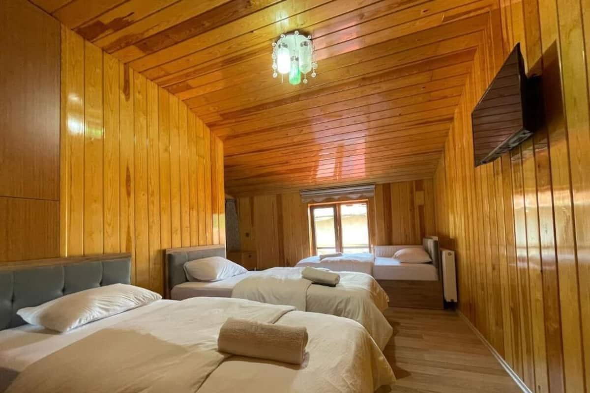 A hotel room with wooden walls and ceiling, two beds with white linens, a small window, and a wall-mounted TV.