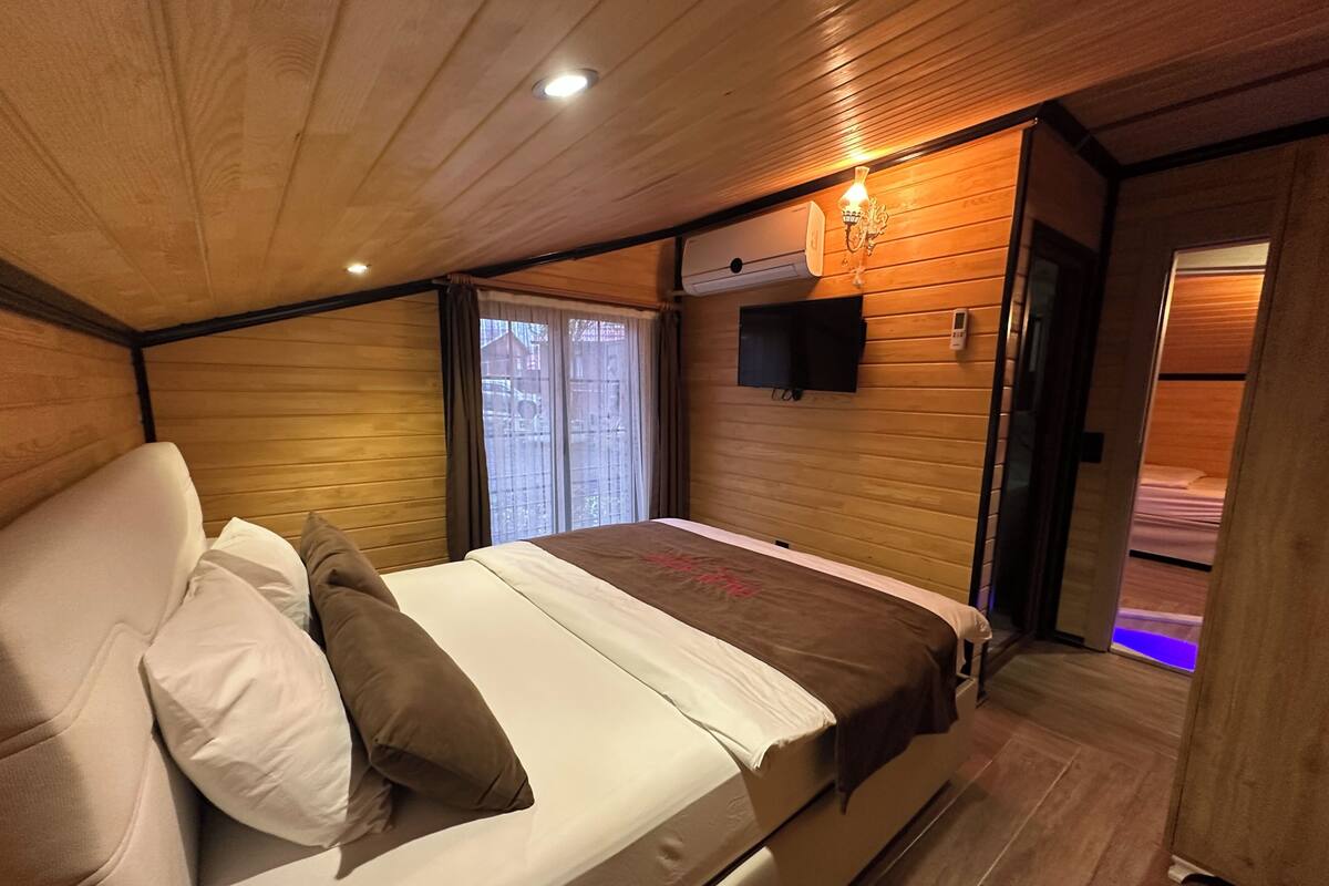 A bedroom with a bed, pillows, a mounted TV, and a window with curtains.