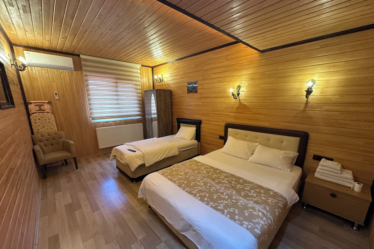 A room with two beds, a chair, a wardrobe, and a nightstand with a lamp.