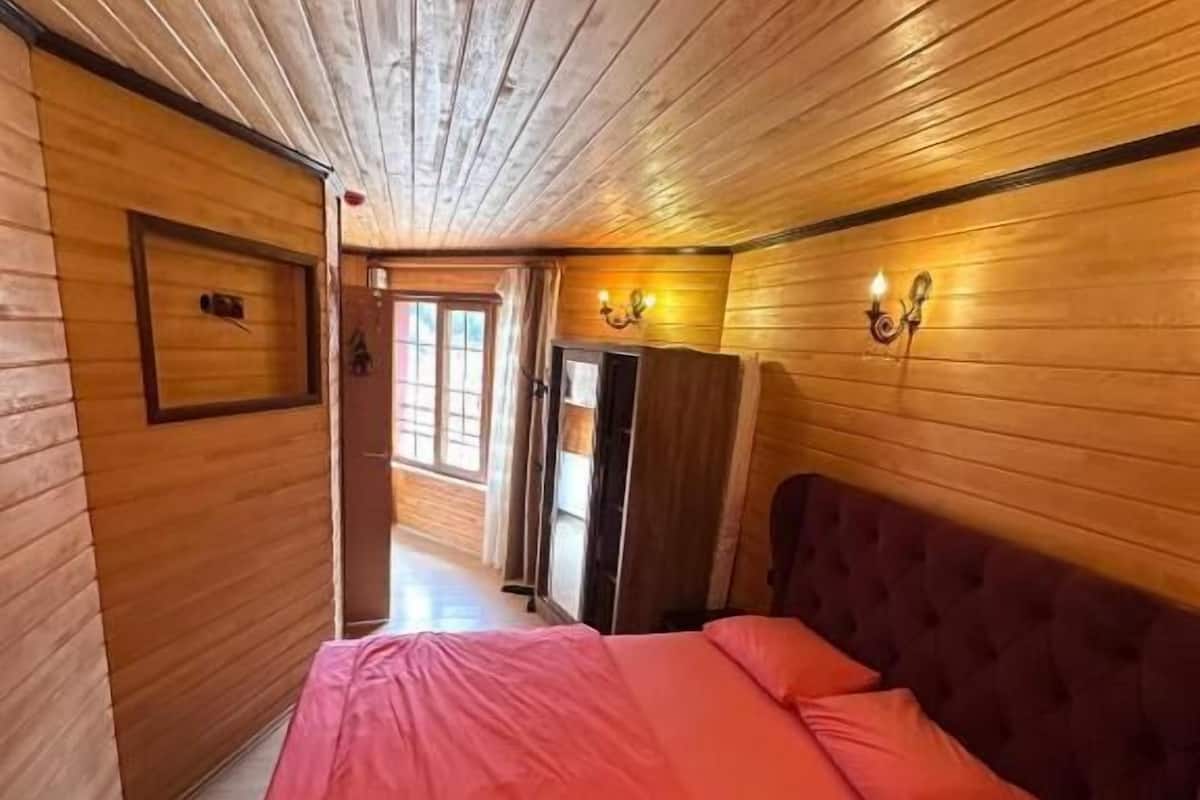 A wooden-paneled room with a bed, a door, and a wall-mounted light fixture.