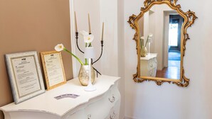 Un aparador blanco con diplomas enmarcados, un florero con una flor blanca y un espejo dorado decorado en la pared.