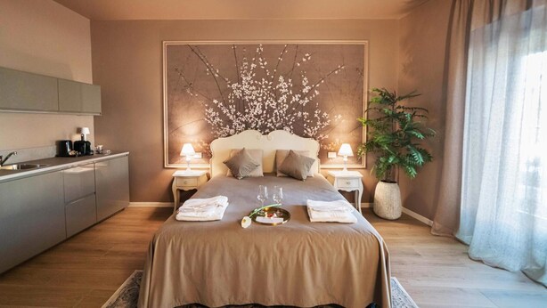 Un dormitorio con cama, mesitas de noche, una planta en maceta y una obra de arte en la pared.
