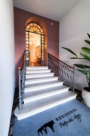 Eine Treppe mit Metallgeländer, einem Blumentopf und einer Fußmatte mit Schrift.