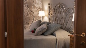 Ein Schlafzimmer mit Bett, Kissen, einer Lampe, einem Schminktisch und einer Wand mit floralem Muster.