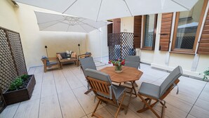 Eine Terrasse im Freien mit einem Holztisch und Stühlen, einem weißen Sonnenschirm und einem Holzzaun.