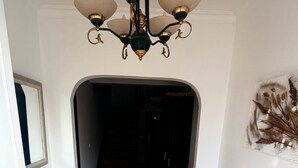 Un couloir orné d’un lustre, d’un miroir, d’un escalier et d’une plante fixée au mur.
