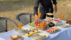 Un chef sirve comida en una mesa de comedor al aire libre, con diversas frutas, pan y bebidas.