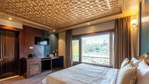 Un dormitorio con una cama grande, televisión, escritorio con ordenador, ventana con vistas y techo decorativo.
