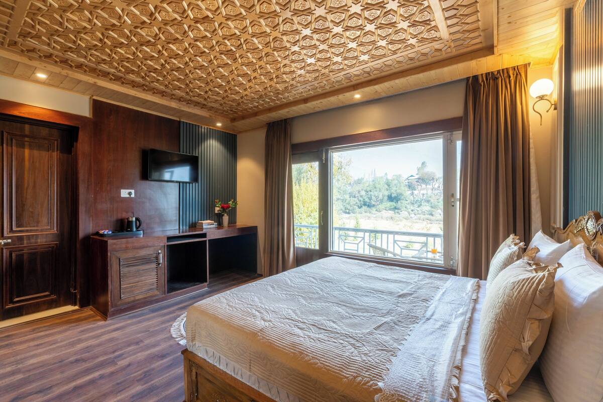 Quarto com uma cama grande, uma televisão, uma escrivaninha com um computador, uma janela com vista e teto decorativo.