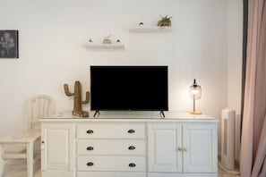 Et hvidt skab med skuffer, et fladskærms-tv, en kaktus og en lille lampe.