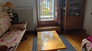 Ein gemütliches Wohnzimmer mit Sofa, Couchtisch, Schrank und Blick durch ein Fenster.