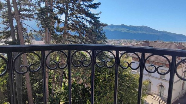 Ein Balkon mit schmiedeeisernem Geländer mit Blick auf eine Stadtlandschaft, mit Gebäuden und einem Berg in der Ferne.