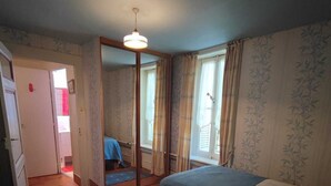 Ein Zimmer mit zwei Betten, einem Spiegel, einer Tür zu einem anderen Zimmer und einer Deckenleuchte.