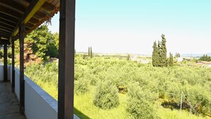 A covered outdoor area with a view of a green landscape and distant buildings. - Apartment 'The Rustic Archontiko' with Sea View (Kranidi)