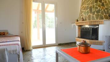 Una habitación con chimenea de piedra, una cama con cubrecama estampado y un ventanal corredero que da a un espacio exterior.