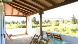 A covered patio with a table and chairs, a view of a green landscape, and a wooden ceiling structure. - Apartment 'The Rustic Archontiko' with Sea View (Kranidi)