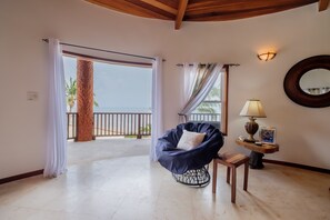 A room with a view of the sea, a bean bag chair, a lamp, and a wooden table. - Your Beachfront Escape on Ambergris Caye Indigo 1B (San Pedro - North)