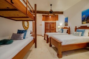 A room with two wooden bunk beds, a ceiling fan, and a wooden door. - Your Beachfront Escape on Ambergris Caye Indigo 1B (San Pedro - North)