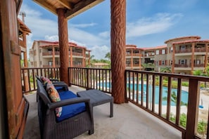 A balcony with wicker furniture and a view of a swimming pool and buildings. - Your Beachfront Escape on Ambergris Caye Indigo 1B (San Pedro - North)
