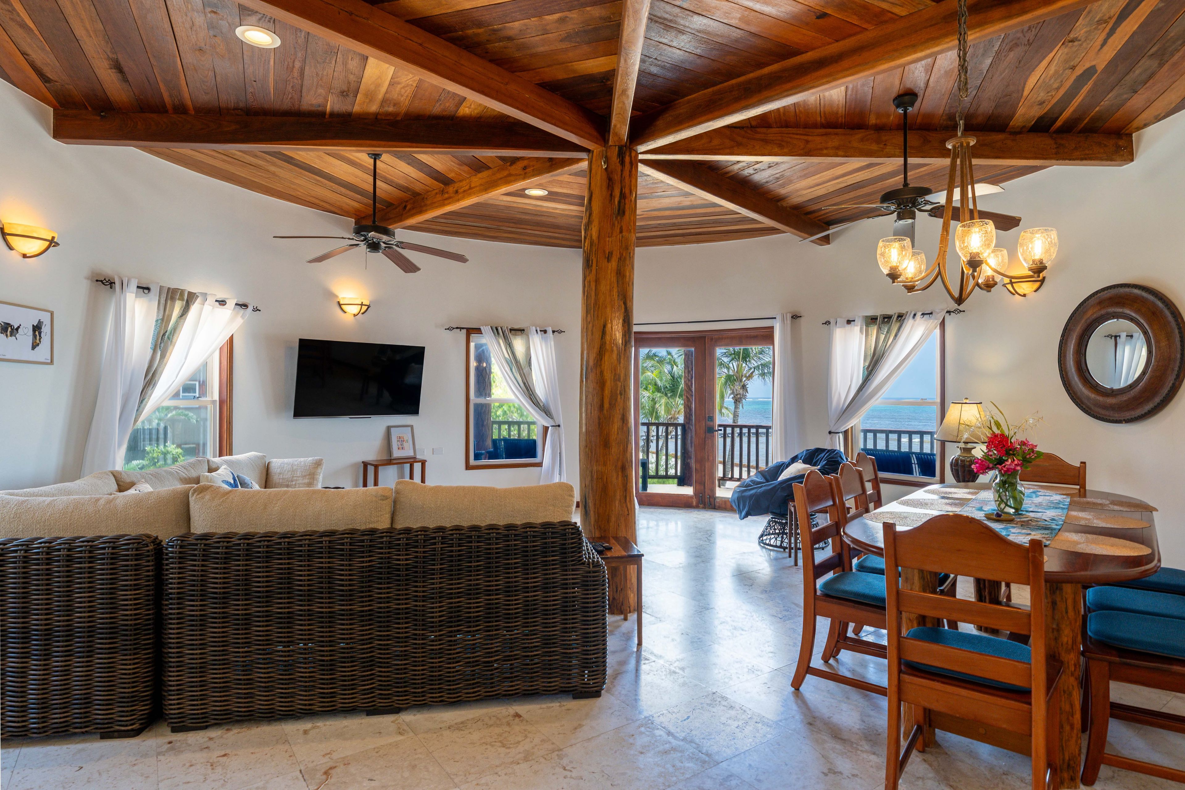 A spacious living area with a high ceiling, a large sofa, a dining table with chairs, and a television mounted on the wall.