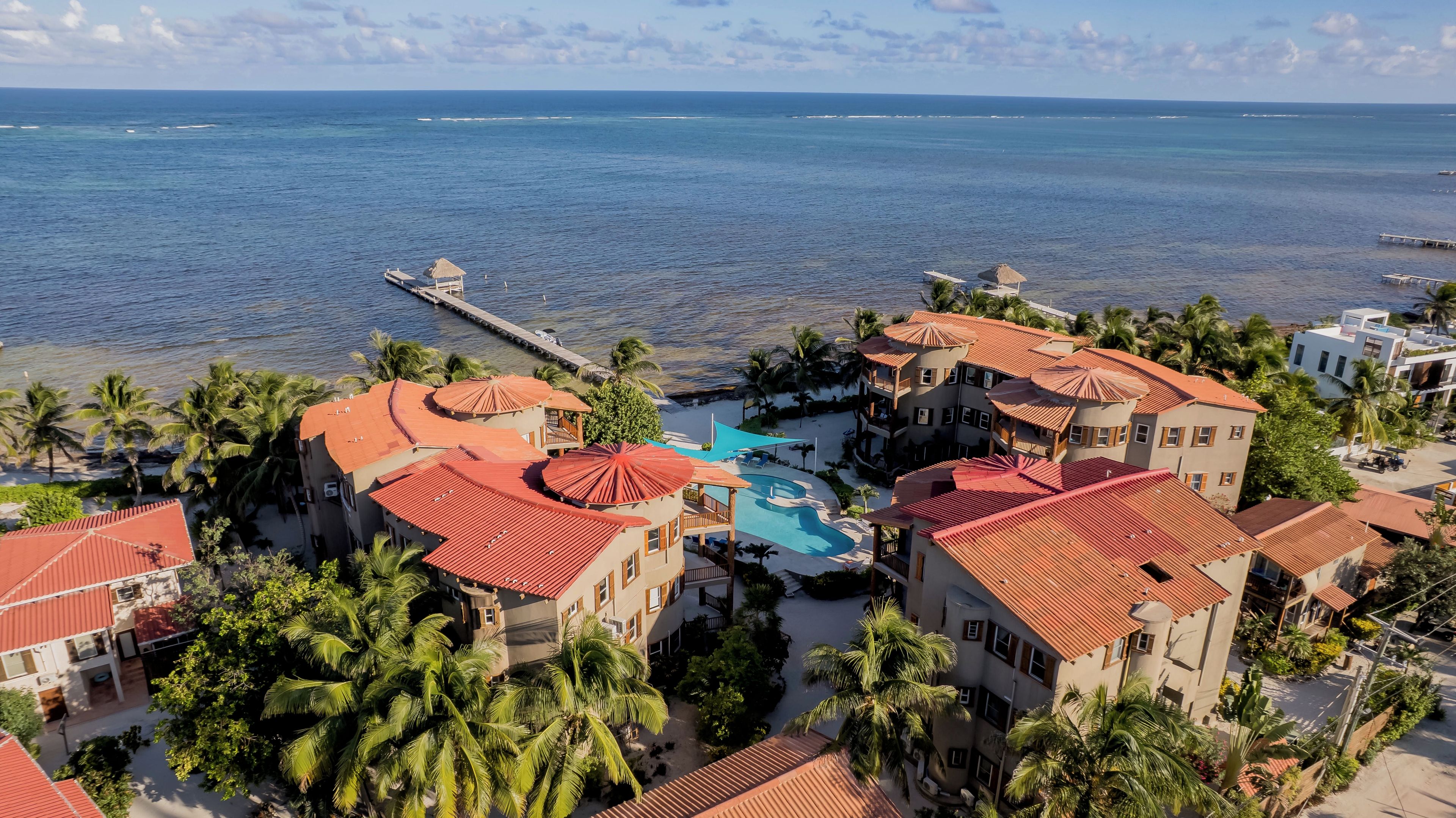 Un resort con varias edificaciones, piscina y un muelle que se adentra en el mar.