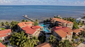 Ein Resort mit mehreren Gebäuden, einem Schwimmbad und einer Pier, die ins Meer hinausführt.