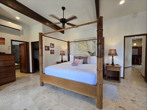 Un letto a baldacchino con una ventola a soffitto, un comodino con una lampada, un quadro e vista sulla cucina.