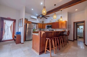 Une cuisine avec des meubles en bois, un coin bar avec des tabourets, un ventilateur de plafond et des luminaires suspendus.