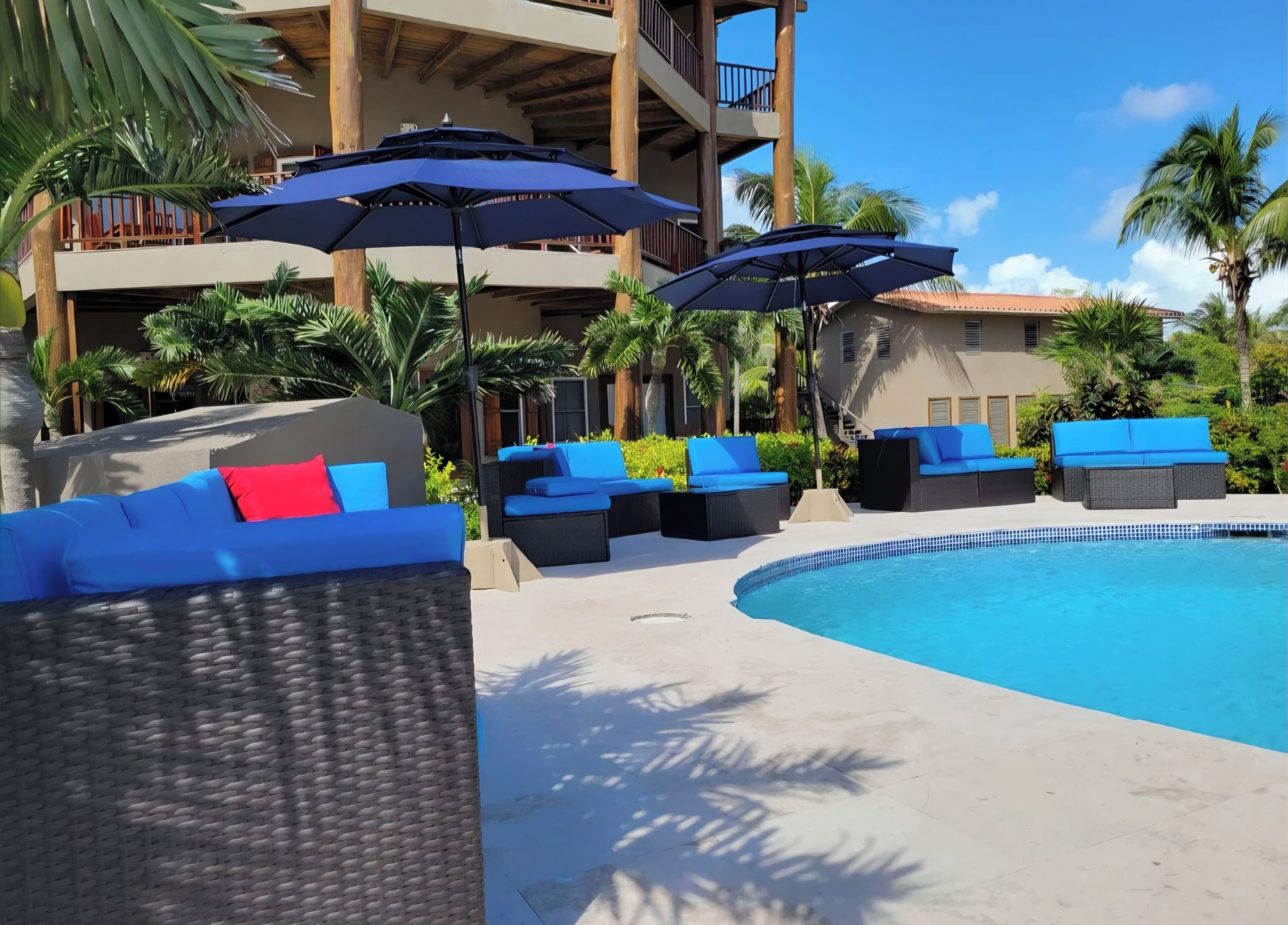 A poolside area with wicker lounge chairs, blue and red cushions, and umbrellas.