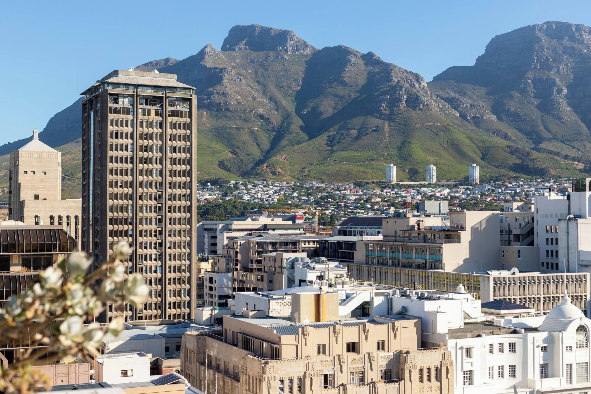 A cityscape with a prominent building, a mountain range, and a densely packed urban area.