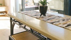 A modern dining area with a long table, wicker chairs, and a potted plant. - Central Cape Town Apt With Views (Cape Town)