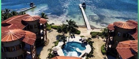 Un resort con varias edificaciones, una piscina y un muelle que se adentra en el océano.