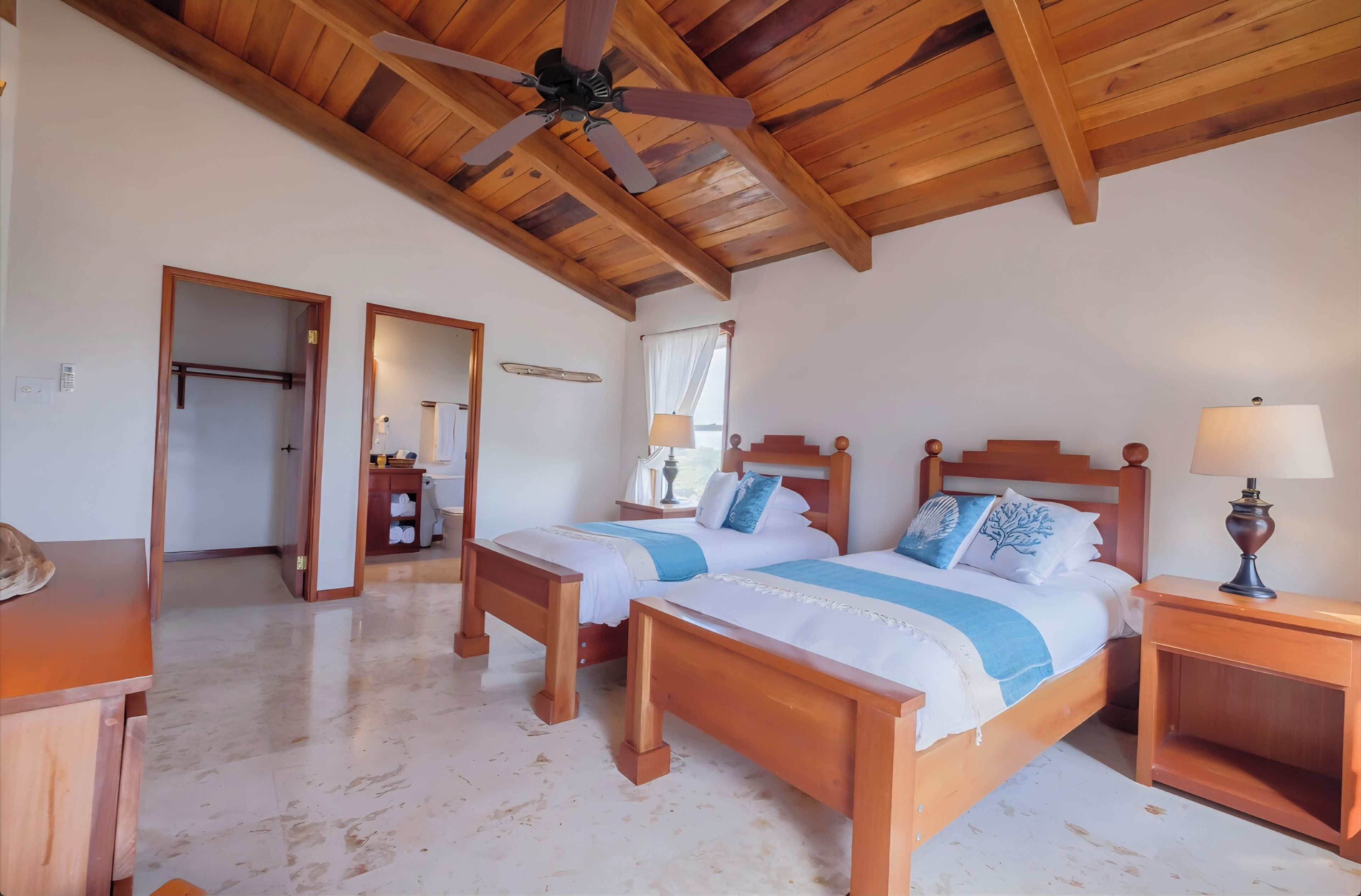 A bedroom with two wooden beds, a ceiling fan, and a nightstand with a lamp.