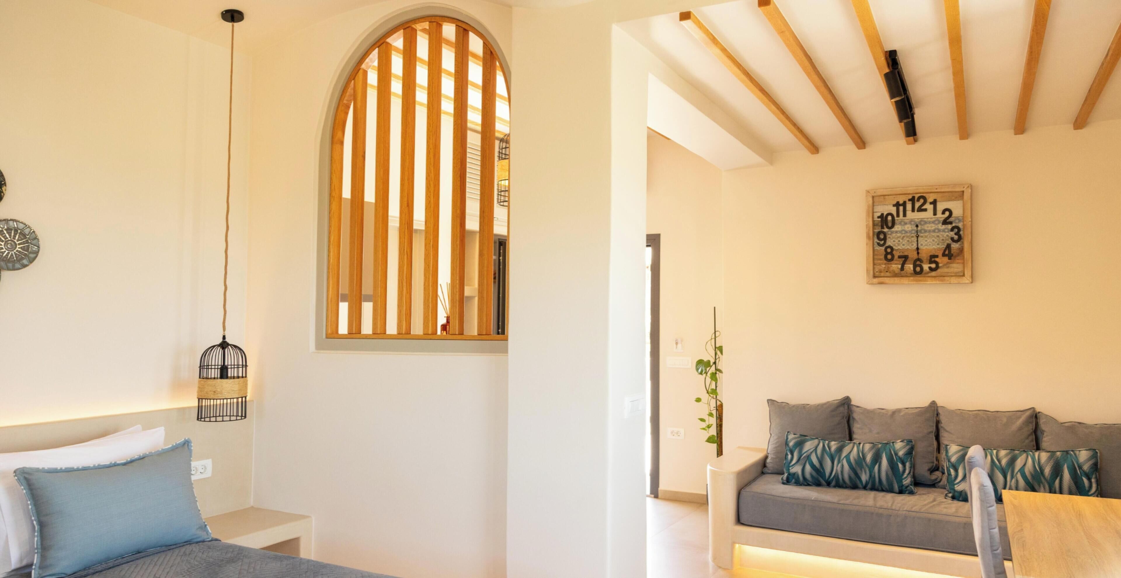 A room with a bed, a wooden slat window, a wall clock, and a sofa.