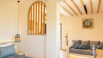 A room with a bed, a wooden slat window, a wall clock, and a sofa.