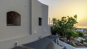 Un edificio moderno con techo plano, una pequeña ventana arqueada y vista a un atardecer sobre un paisaje costero.