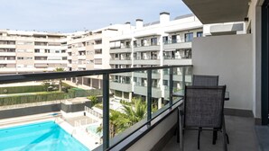 A balcony with a view of a swimming pool, a chair, and a building with multiple balconies. - Live Like a Local- Cozy 3BR in Suite Mijas (Las Lagunas de Mijas)