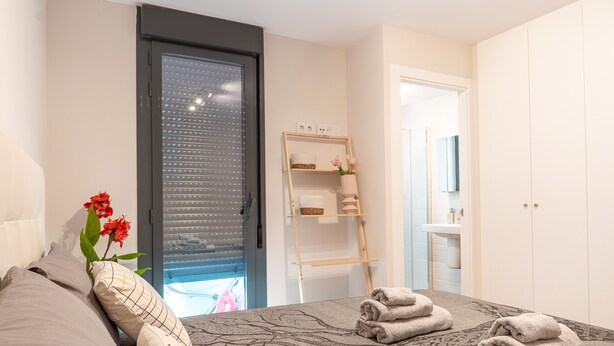 A bedroom with a bed, a wooden ladder, a shelf with towels, and a door leading to a bathroom. - Live Like a Local- Cozy 3BR in Suite Mijas (Las Lagunas de Mijas)