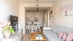 A modern living room with a grey sofa, a wooden coffee table, and a dining area with a glass table and chairs. - Live Like a Local- Cozy 3BR in Suite Mijas (Las Lagunas de Mijas)