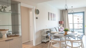 A modern living room with a dining area, a glass cabinet, a wall clock, and a large window. - Live Like a Local- Cozy 3BR in Suite Mijas (Las Lagunas de Mijas)