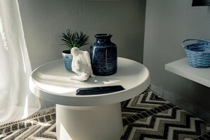 Ein Badezimmer mit einem weißen Waschbecken auf Säule, einer blauen Vase, einer kleinen Topfpflanze, einer weißen Statue und einem blauen gewebten Korb auf einem weißen Regal.