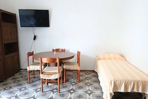 A room with a round wooden table, four chairs, a television mounted on the wall, a bed with a striped blanket, and patterned floor tiles. - RG002 - Bellaria, comfortable two-room apartment with sea view (Bellaria-Igea Marina)