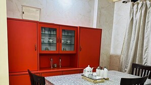 Un coin repas avec une table dressée pour quatre personnes, entouré de meubles rouges aux portes vitrées et doté d’un sol carrelé.