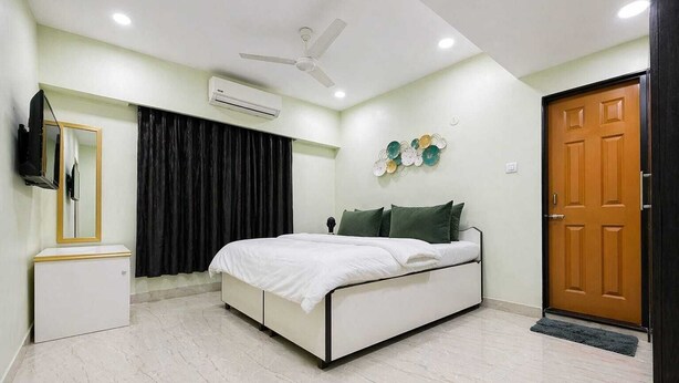 Une chambre à coucher comprenant un lit, une armoire, un miroir, un ventilateur de plafond, un climatiseur et une porte.