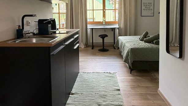 Una habitación compacta con kitchenette, una pequeña mesa, una cama y una ventana con cortinas.