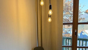 Un comedor con una mesa y sillas, un ventanal que ofrece vistas a un edificio y árboles, y dos bombillas colgantes.