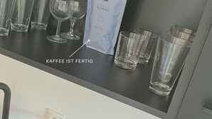 Una cafetera, un paquete de café y varios vasos sobre una encimera.