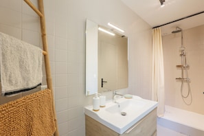 Une salle de bain avec un lavabo blanc, un miroir et une douche.