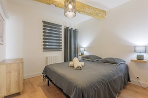 Une chambre Ă coucher comprenant un lit, une table de chevet en bois, une Ă©tagĂšre fixĂ©e au mur et une fenĂȘtre avec des stores.