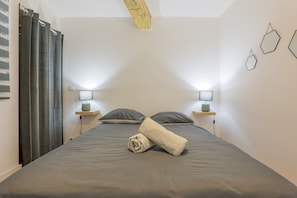 Une chambre Ă coucher avec un lit, deux tables de chevet avec des lampes, une serviette et un rideau.